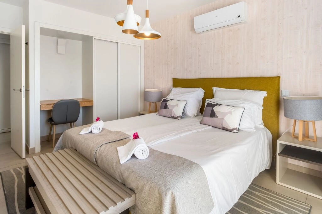 Modern bedroom with twin beds, desk, and air conditioning.