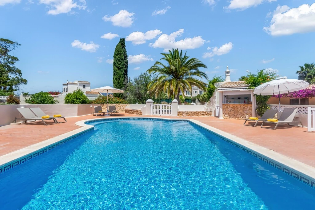 A sunny poolside scene with loungers, umbrellas, and a clear blue sky.
