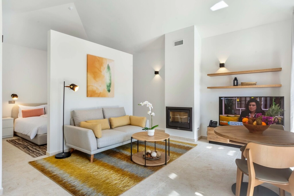 Modern living room with sofa, TV, table, and partially visible bedroom.