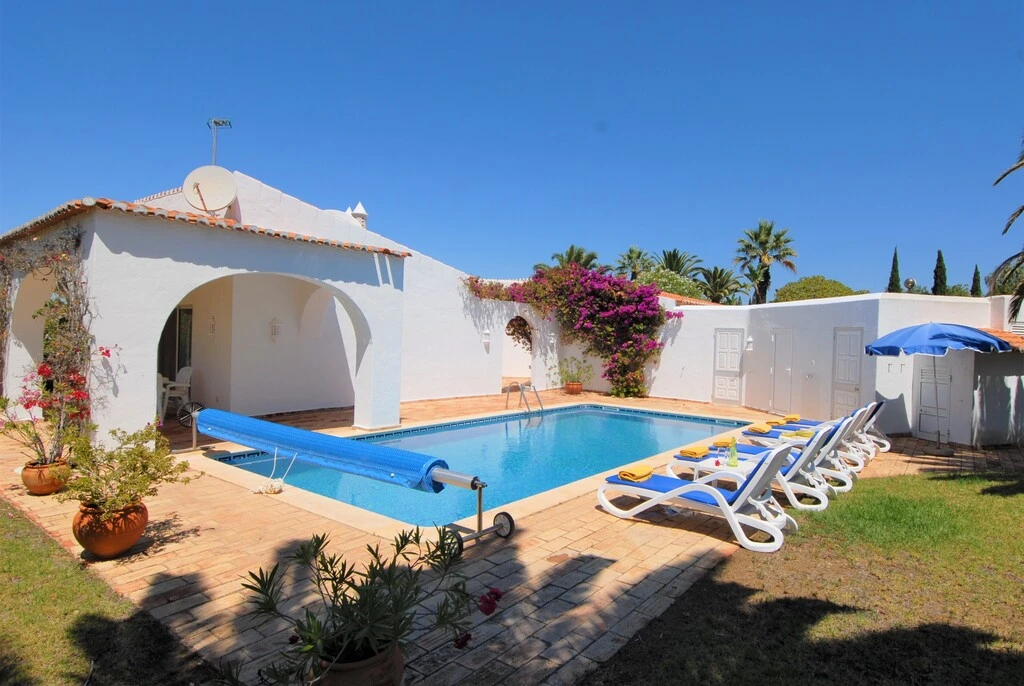 White villa with blue pool, sun loungers, and garden under clear blue sky.