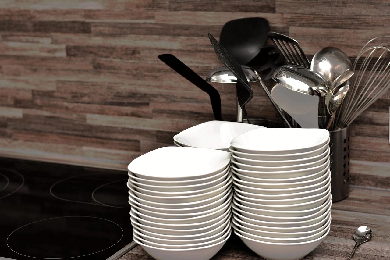 Stacks of white bowls with kitchen utensils in a holder.