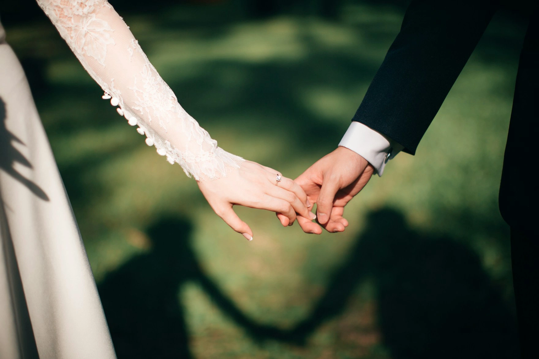 Couple holding hands, casting a heart-shaped shadow on grass.