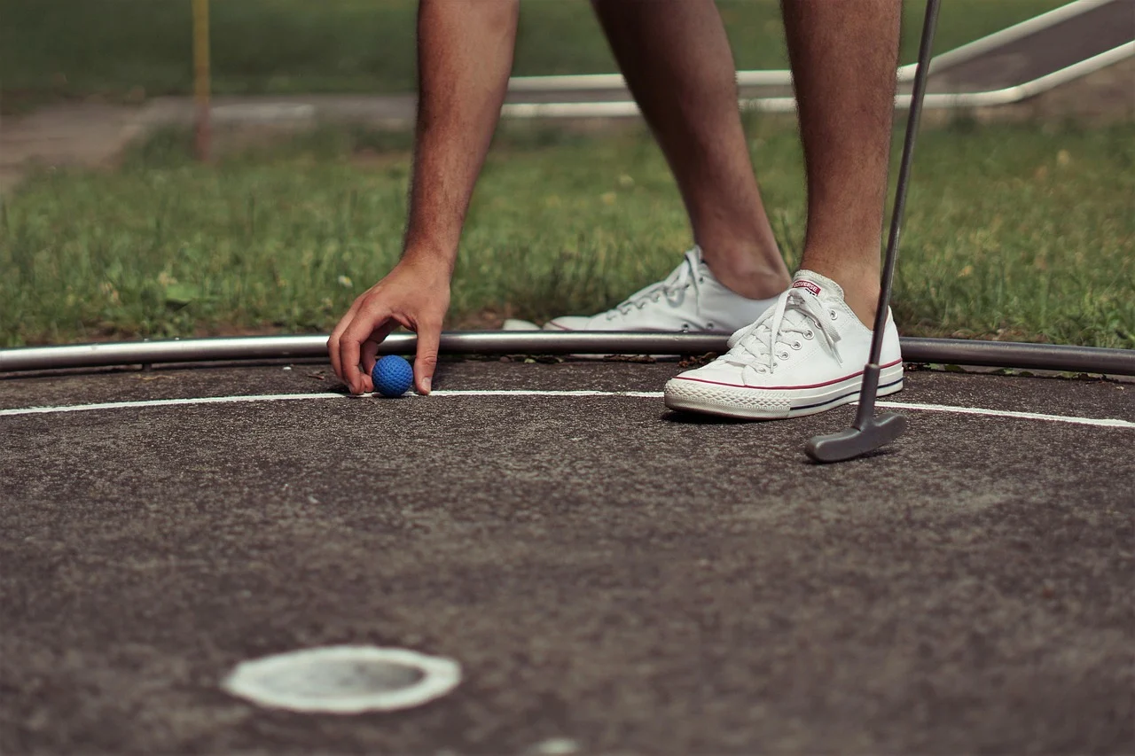 Person placing a blue golf ball on a mini-golf course.
