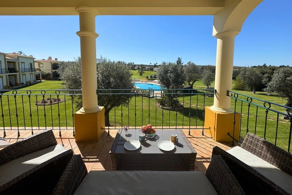 Balcony view of grassy lawn and pool, with outdoor seating and table in foreground.