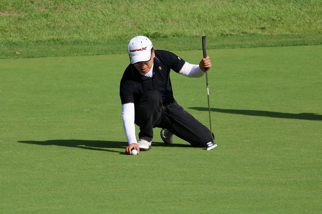 Golfer kneeling and placing ball on the putting green.