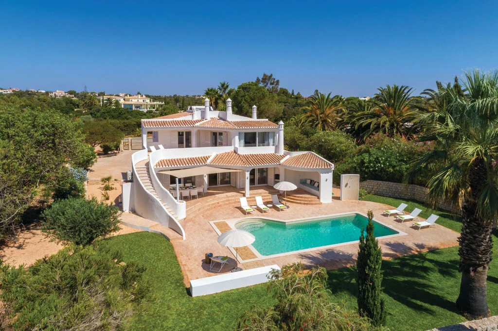 Large villa with a pool, surrounded by palm trees and greenery.