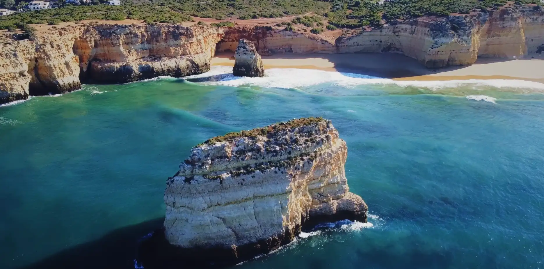 Cliffs and clear ocean with waves crashing onto a sandy beach.