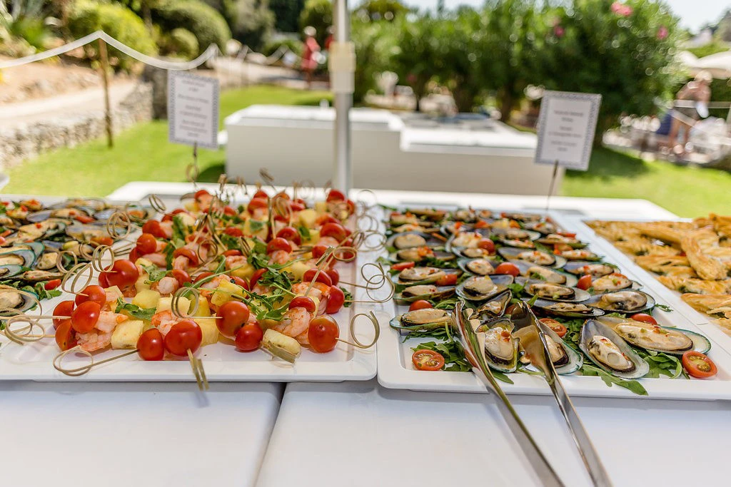 Skewers and mussels displayed on a white tray at an outdoor event.