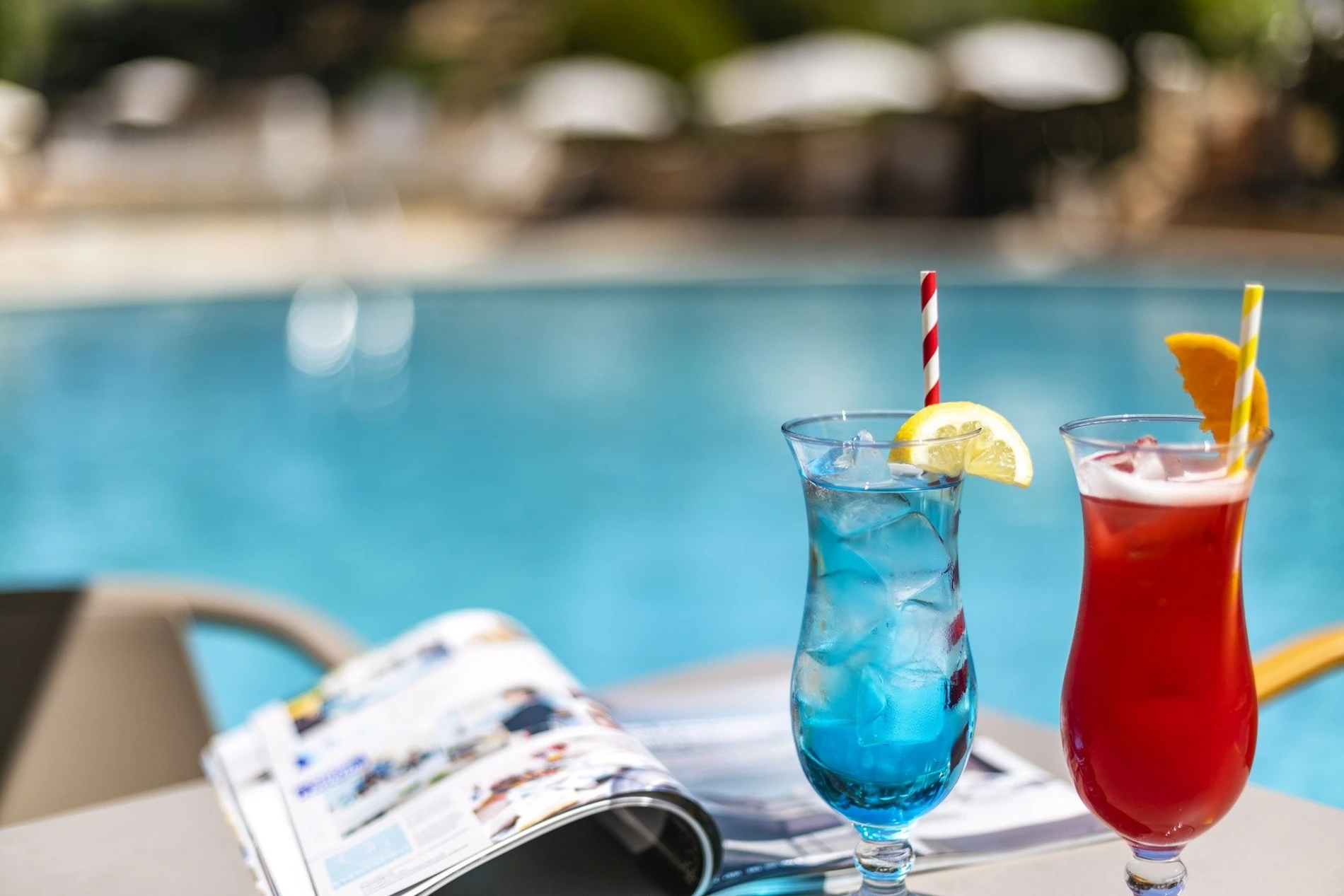 Two colorful cocktails and a magazine by a pool.