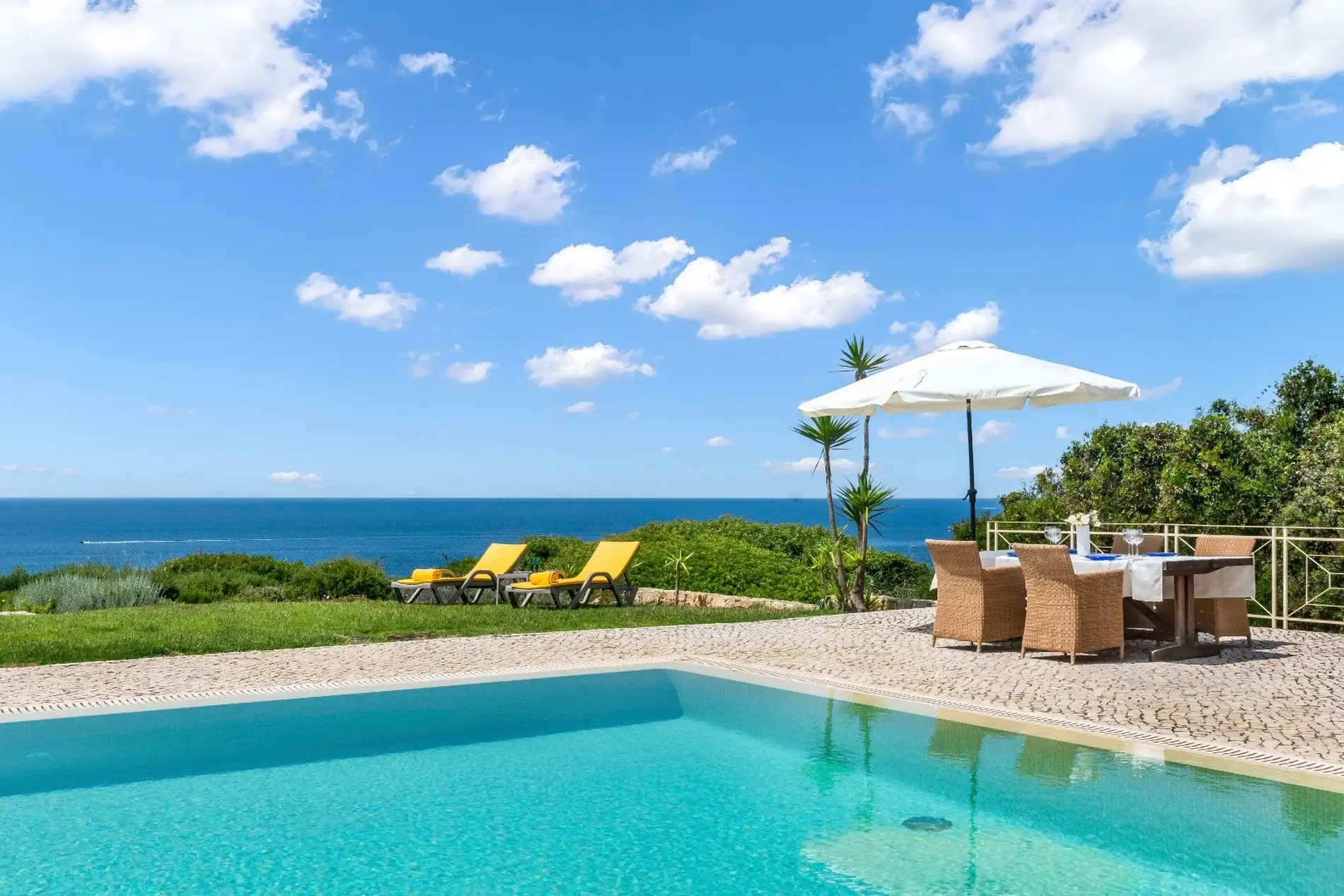 Poolside view with loungers and a dining table overlooking the ocean.