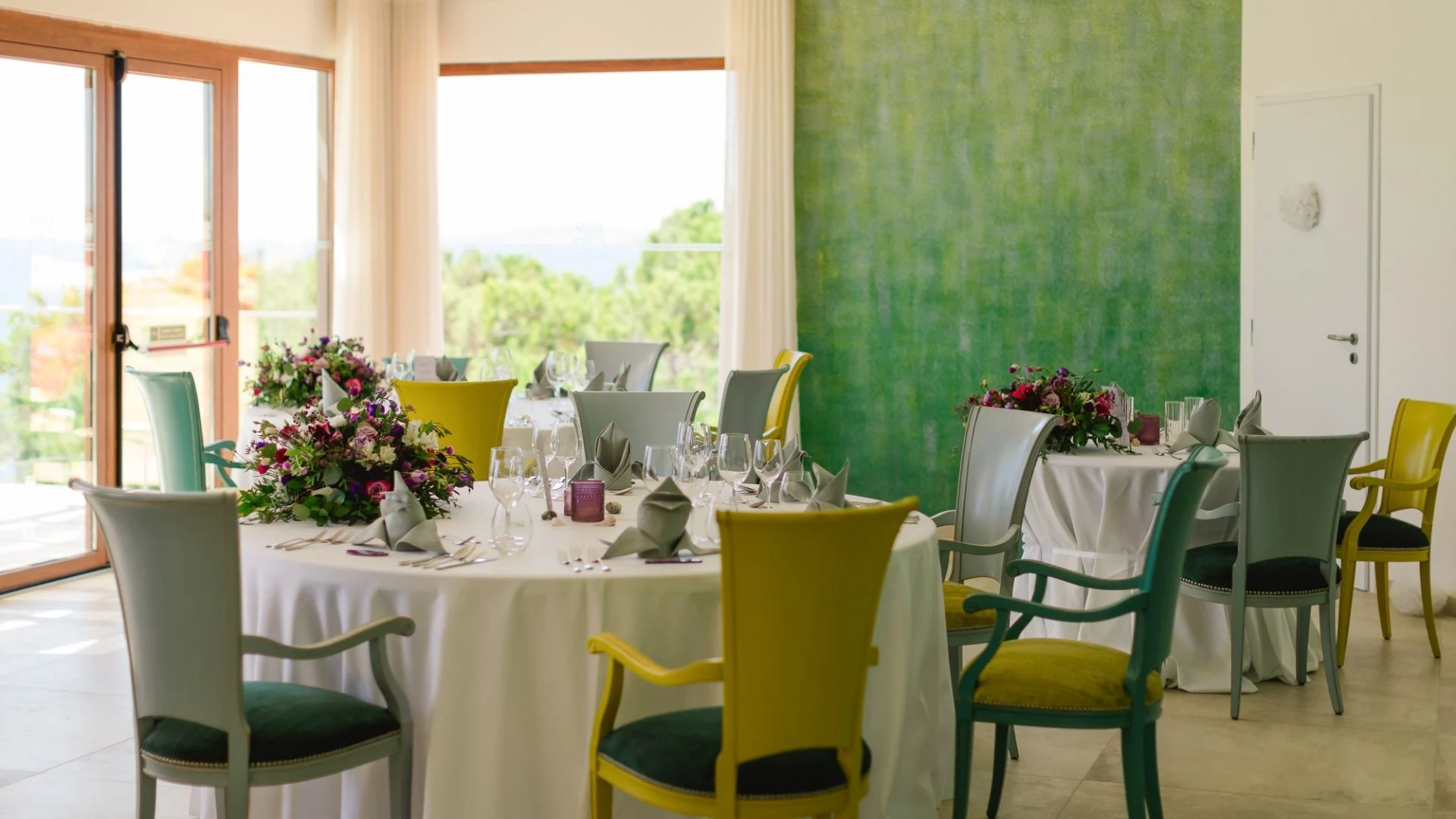 Elegant dining setup with colorful chairs and flower arrangements.