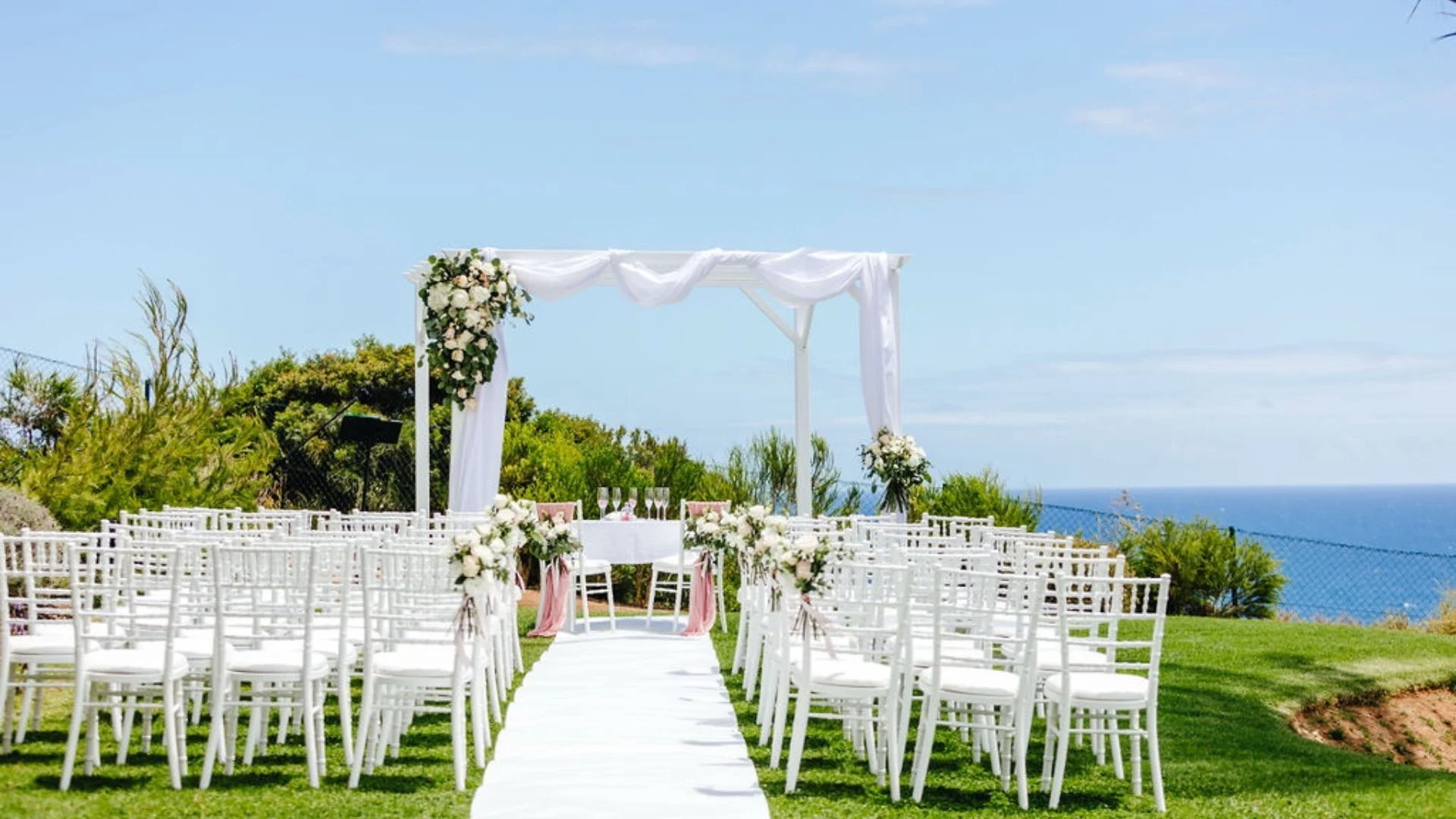 Outdoor wedding setup with white chairs and floral decorations by the ocean.