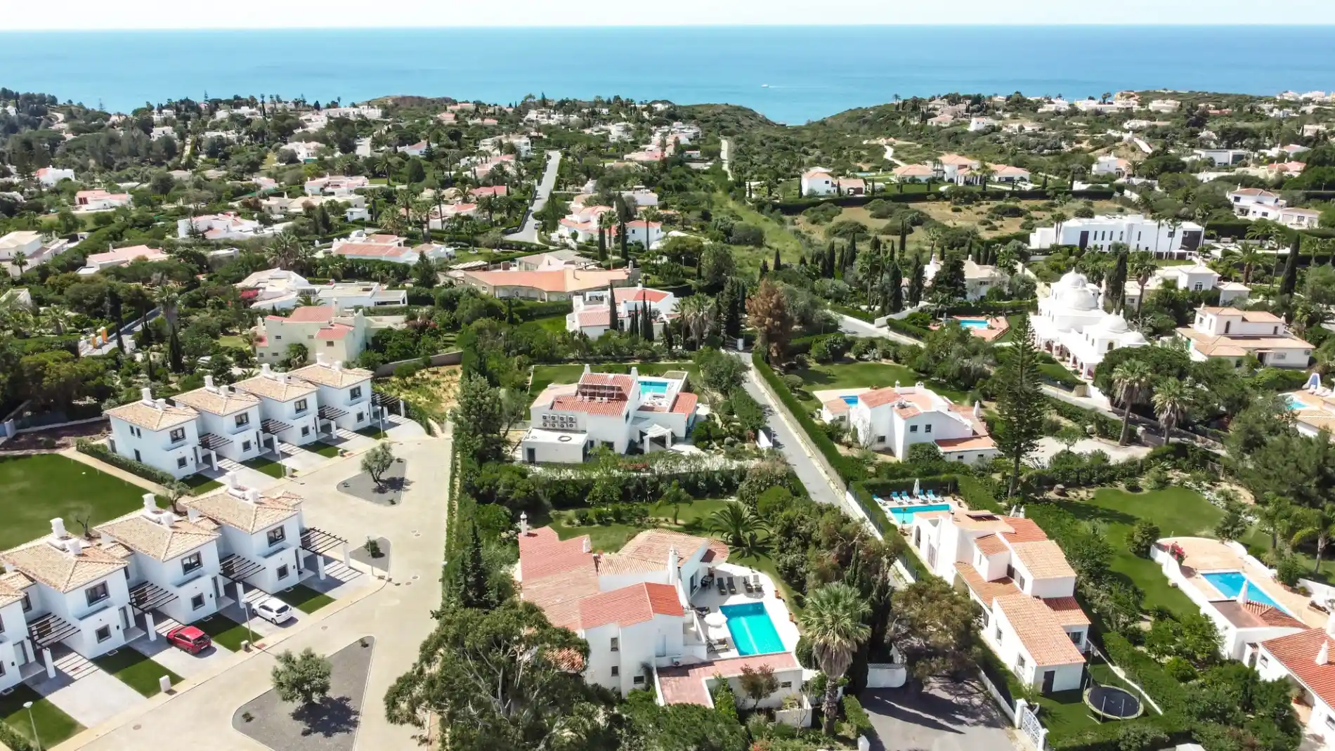 Aerial view of a coastal town with houses, pools, and greenery.
