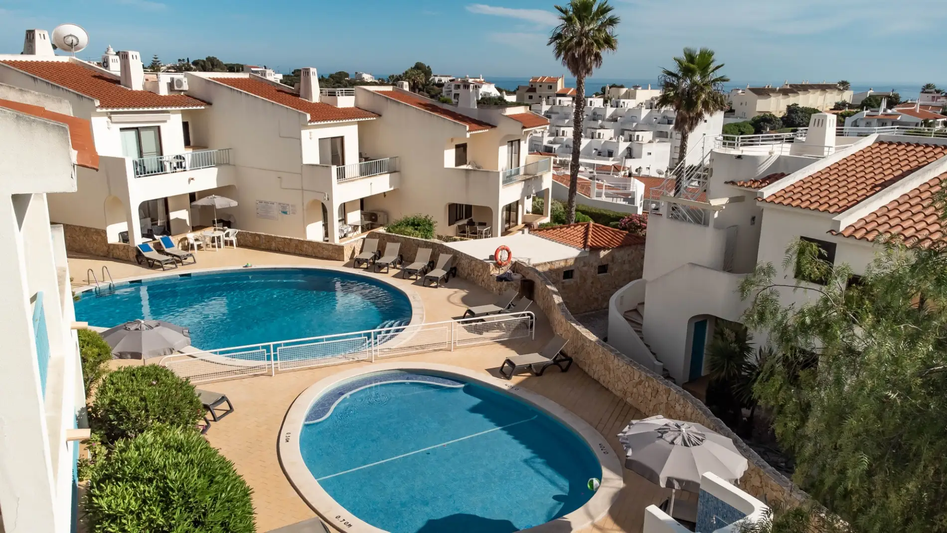 Aerial view of a hotel pool area with loungers and buildings in the background.
