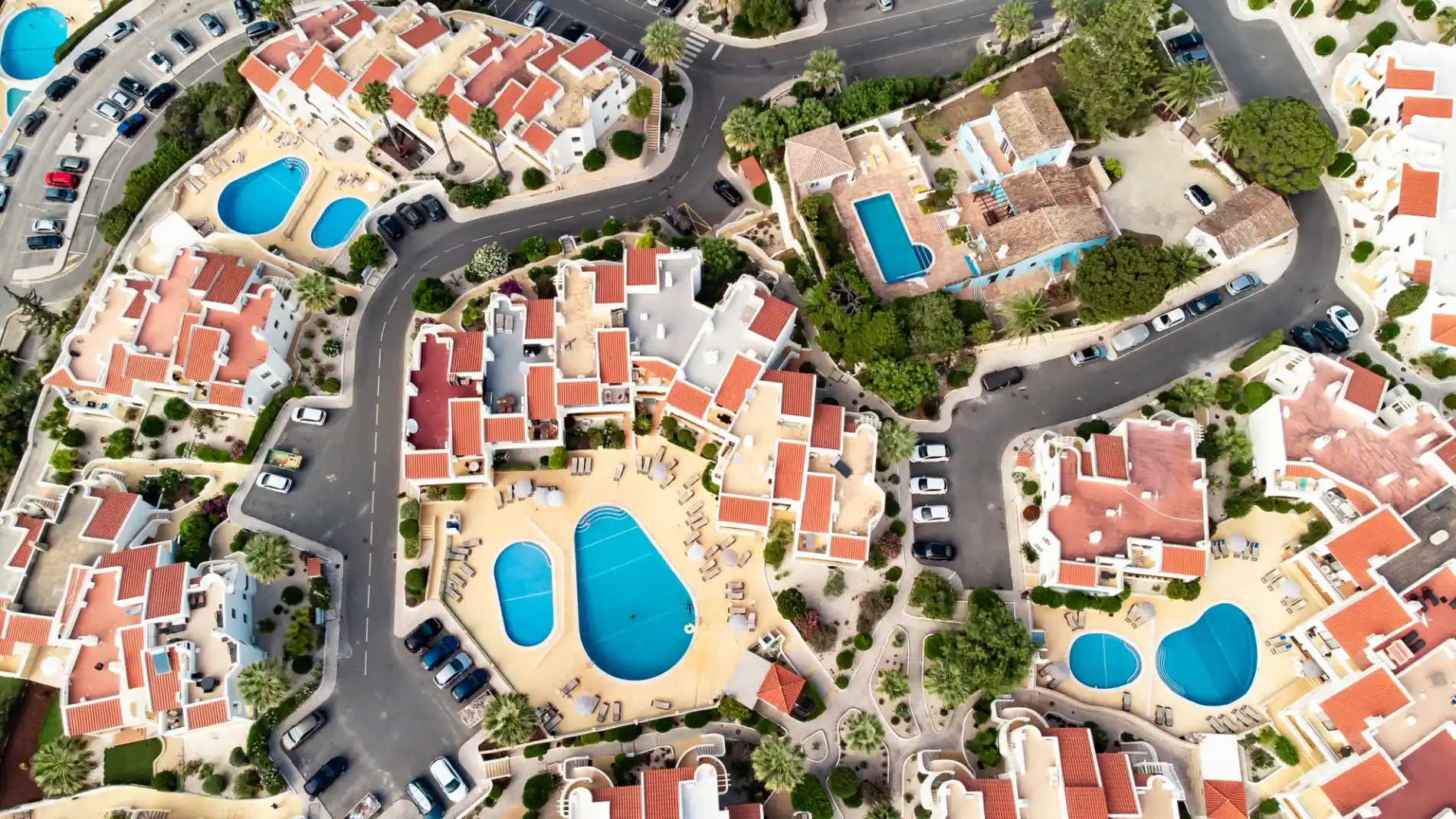Aerial view of a neighborhood with pools and red-roofed houses.