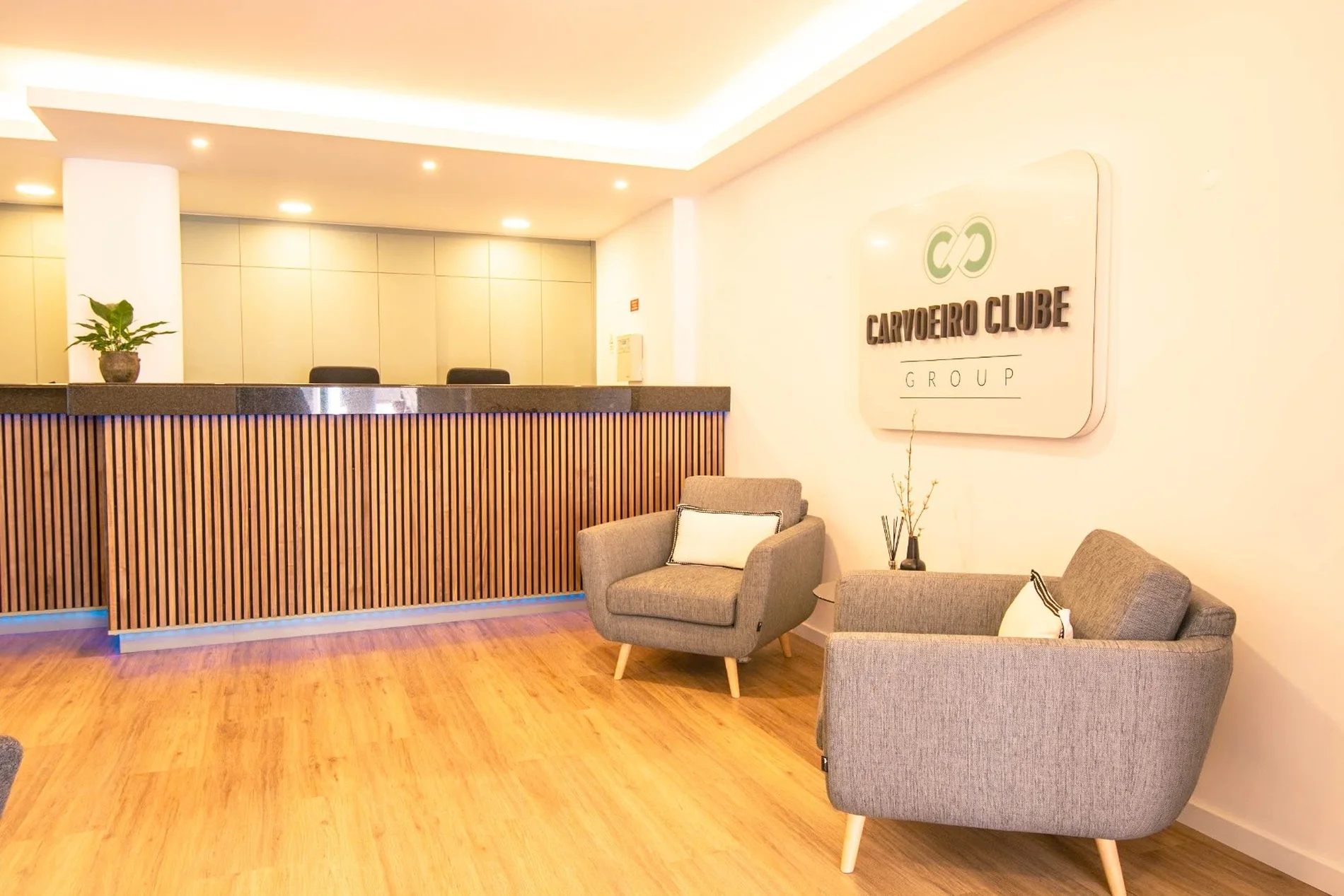 Reception area with a wooden desk and gray chairs on a wooden floor.