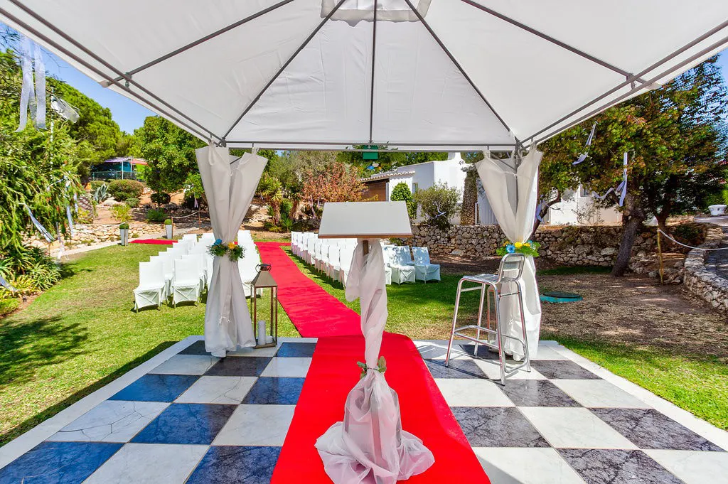 Outdoor wedding setup with red carpet, chairs, and a decorated tent.