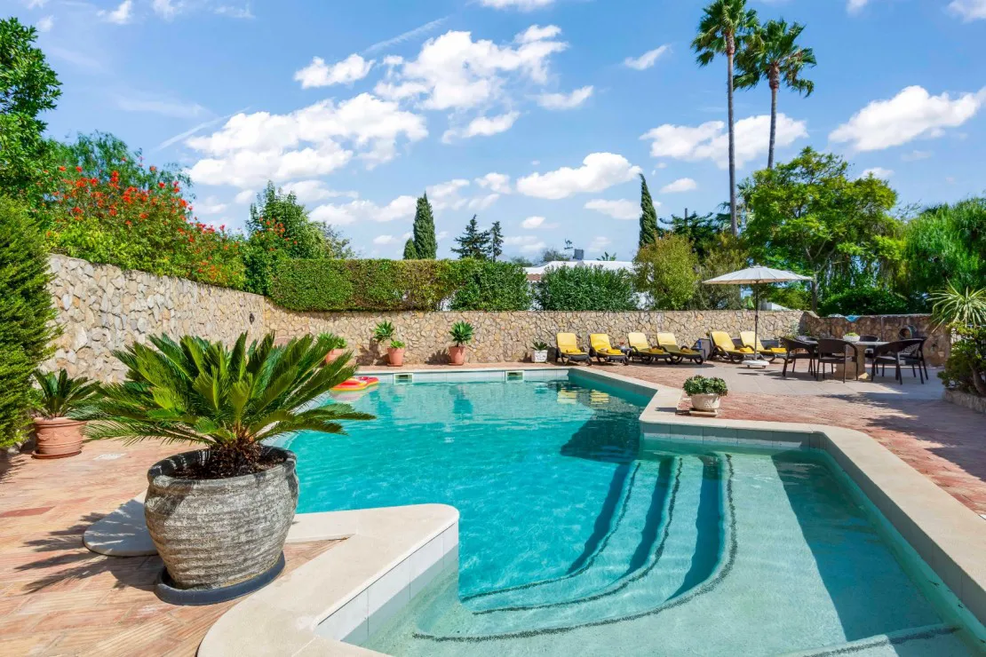 Outdoor pool with lounge chairs, potted plants, and clear blue skies.