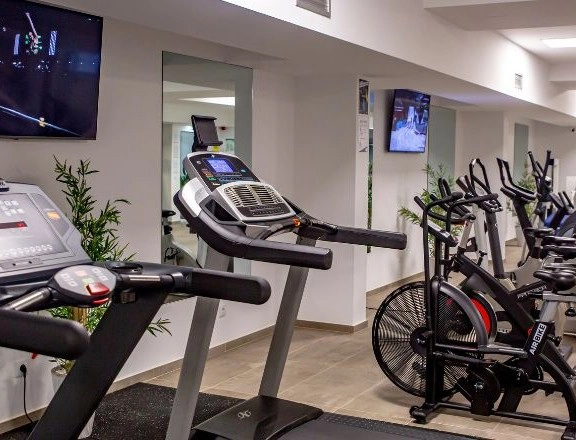Treadmills and exercise bikes in a modern gym with TV screens on walls.