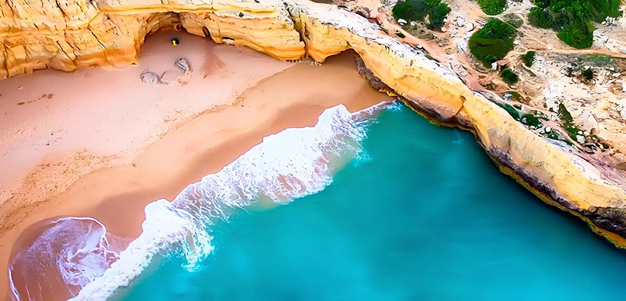 Aerial view of a secluded beach with turquoise water and golden cliffs.