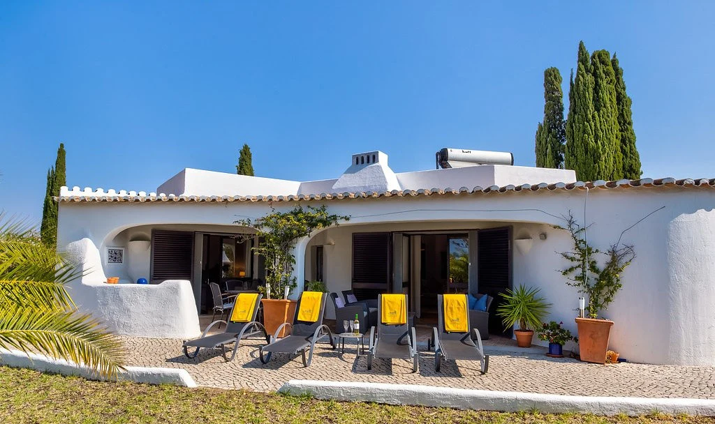 White villa with sun loungers and potted plants in front.