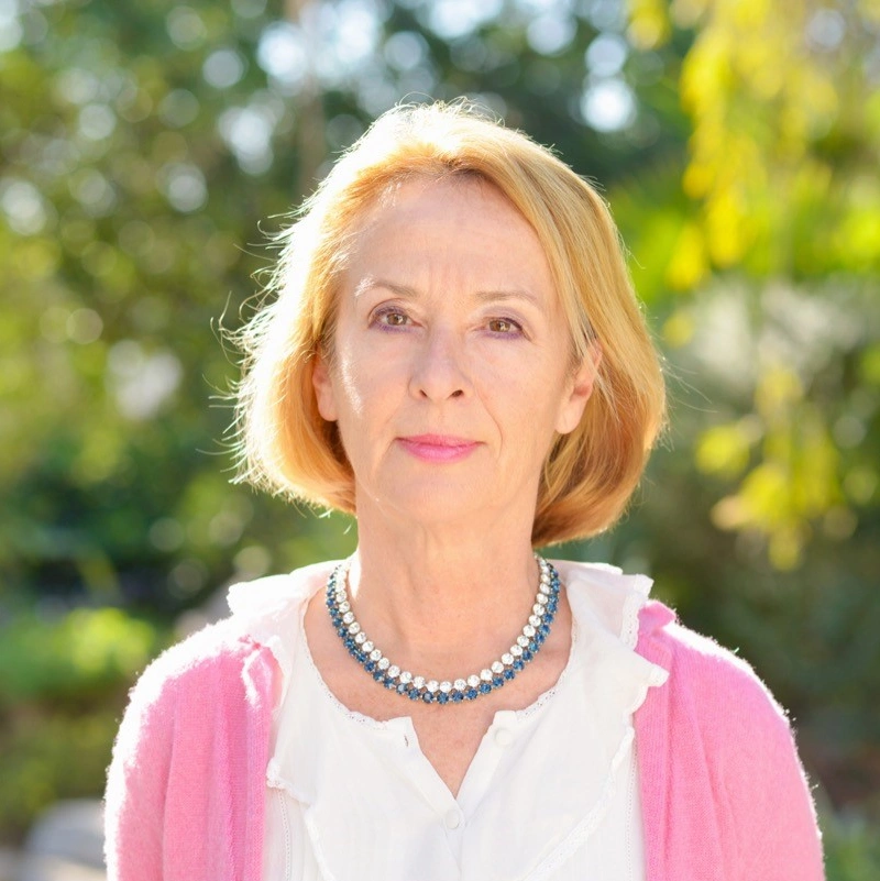 Older woman outdoors, wearing a pink sweater and a beaded necklace.