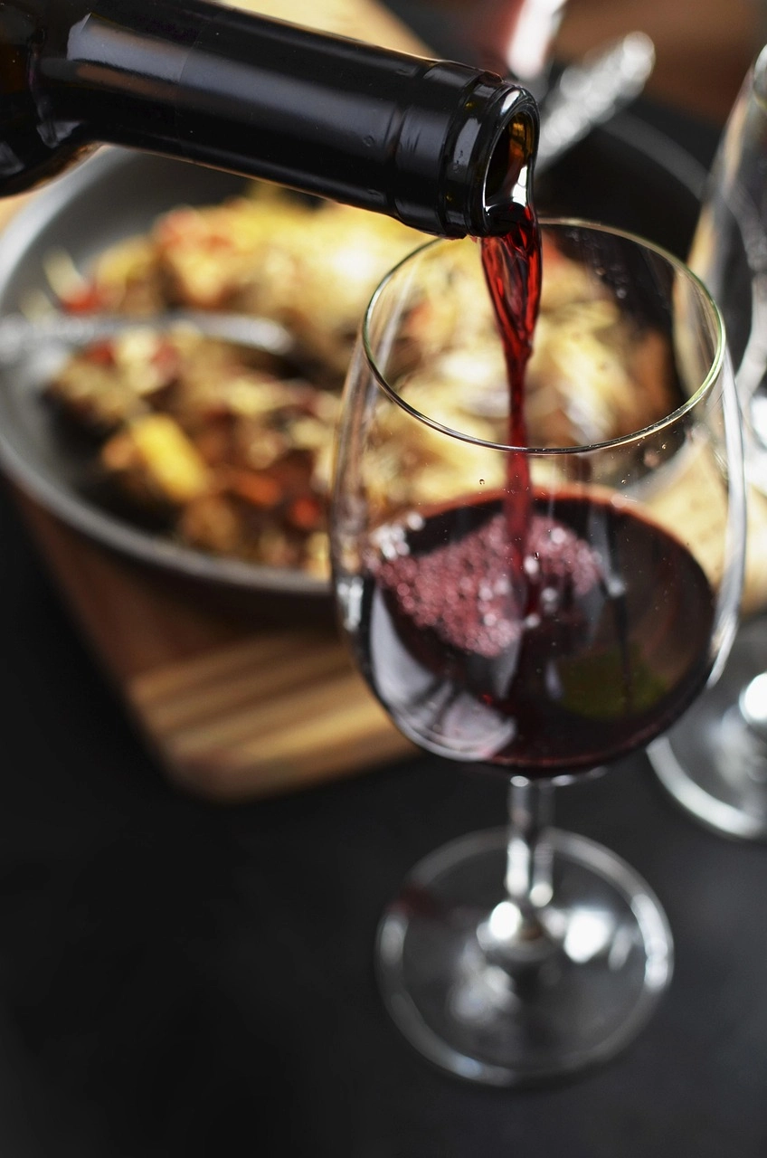 Pouring red wine into a glass near a dish on a wooden board.