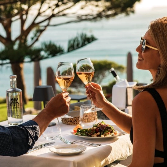 Couple toasting wine glasses at an outdoor seaside dining table.