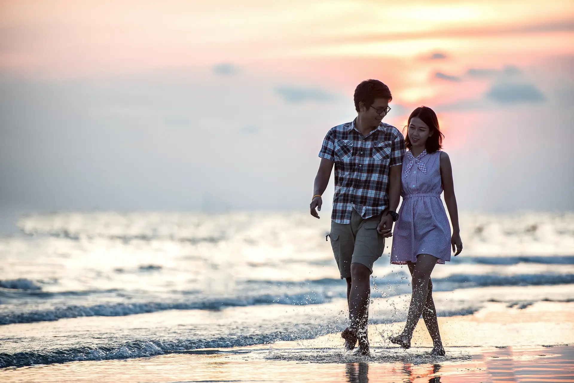 Couple walking hand in hand on the beach at sunset.