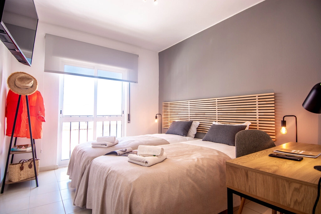 Modern bedroom with twin beds, a desk, and natural light from a window.