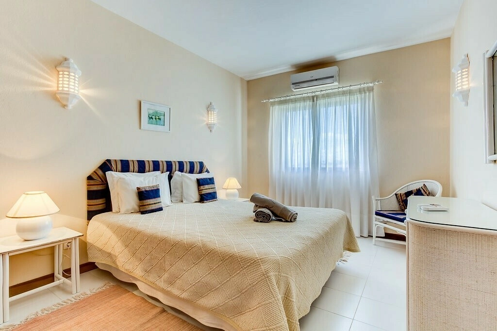 Bright bedroom with a cozy bed, lamps, and a window with sheer curtains.