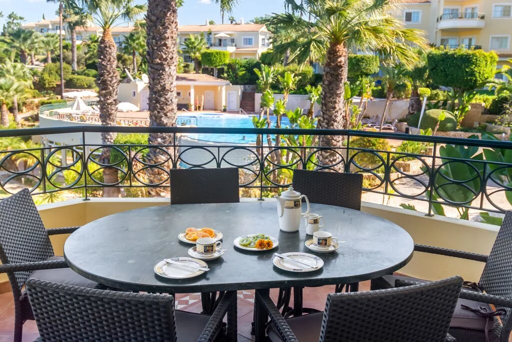 Outdoor dining table with breakfast, overlooking pool and palm trees.