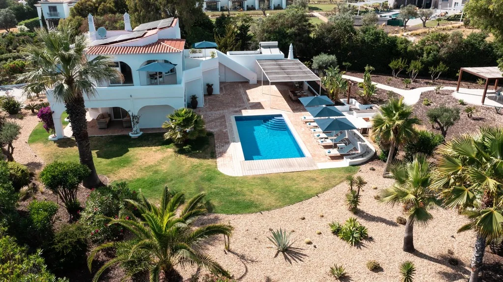 Aerial view of a villa with a pool surrounded by palm trees and gardens.