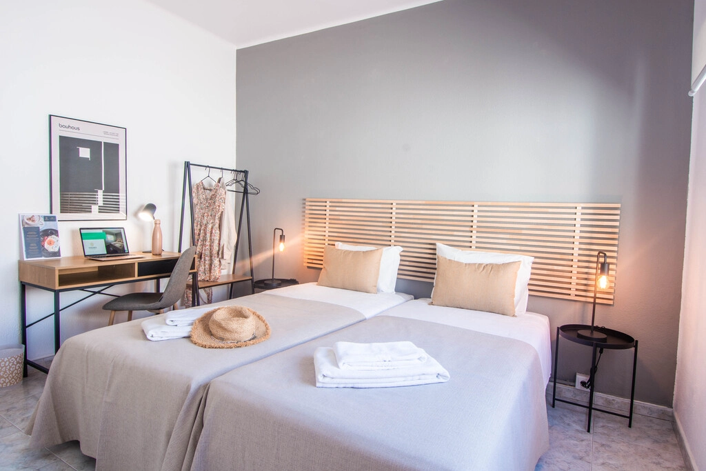 Modern bedroom with twin beds, desk, chair, and hanging clothes.