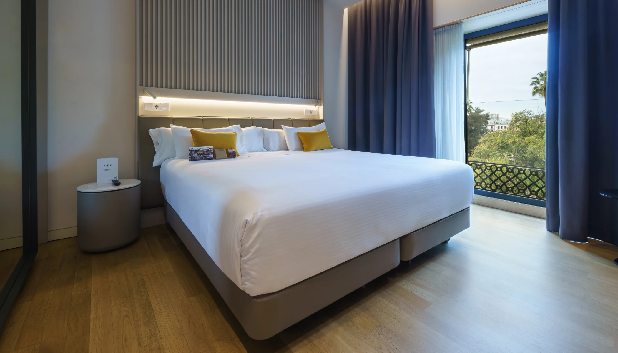 Hab: Cama grande, s&aacute;banas blancas, cojines amarillos, ventana con vista &aacute;rboles.