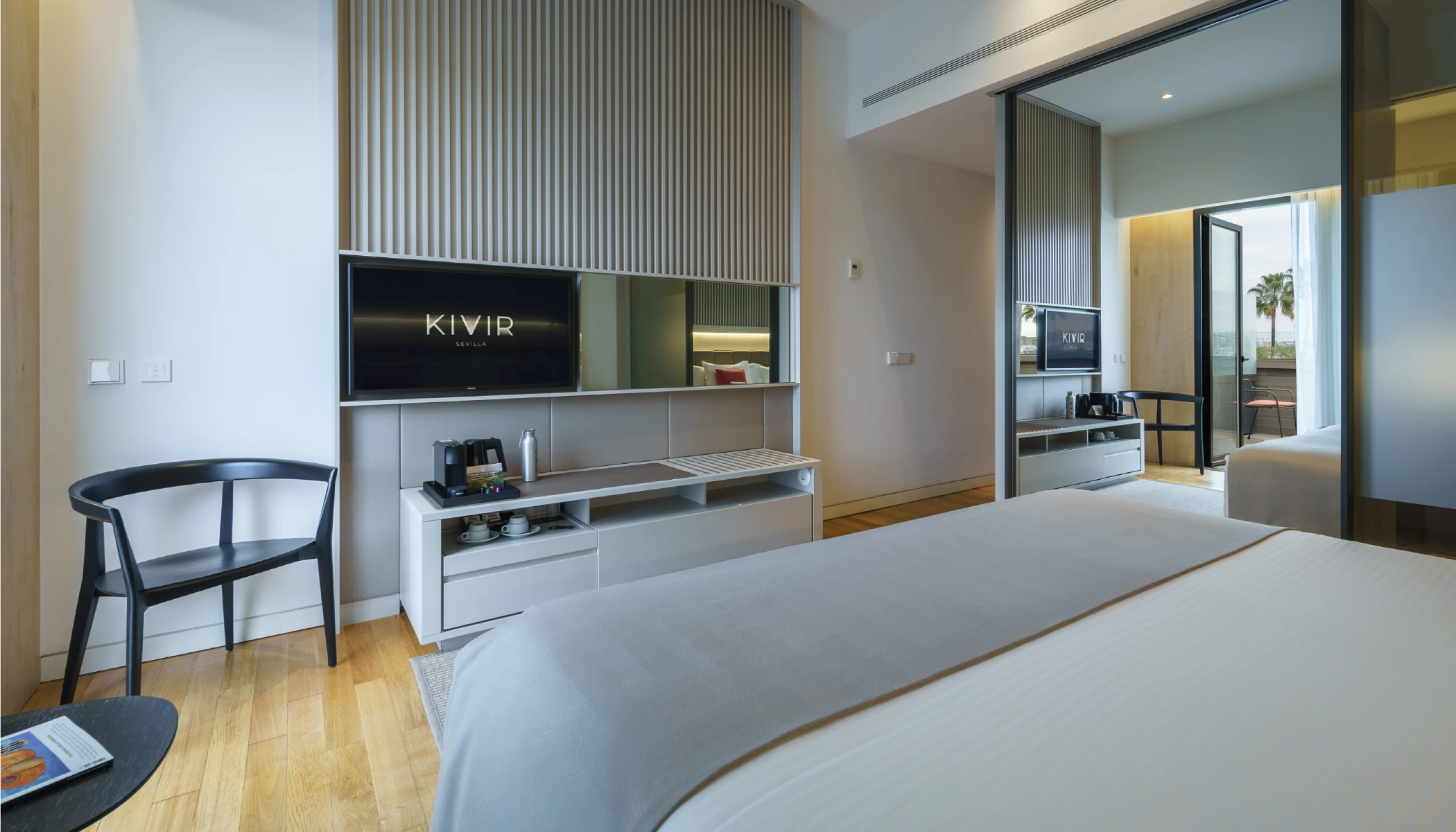 Habitaci&oacute;n de hotel moderna con cama, TV y balc&oacute;n.