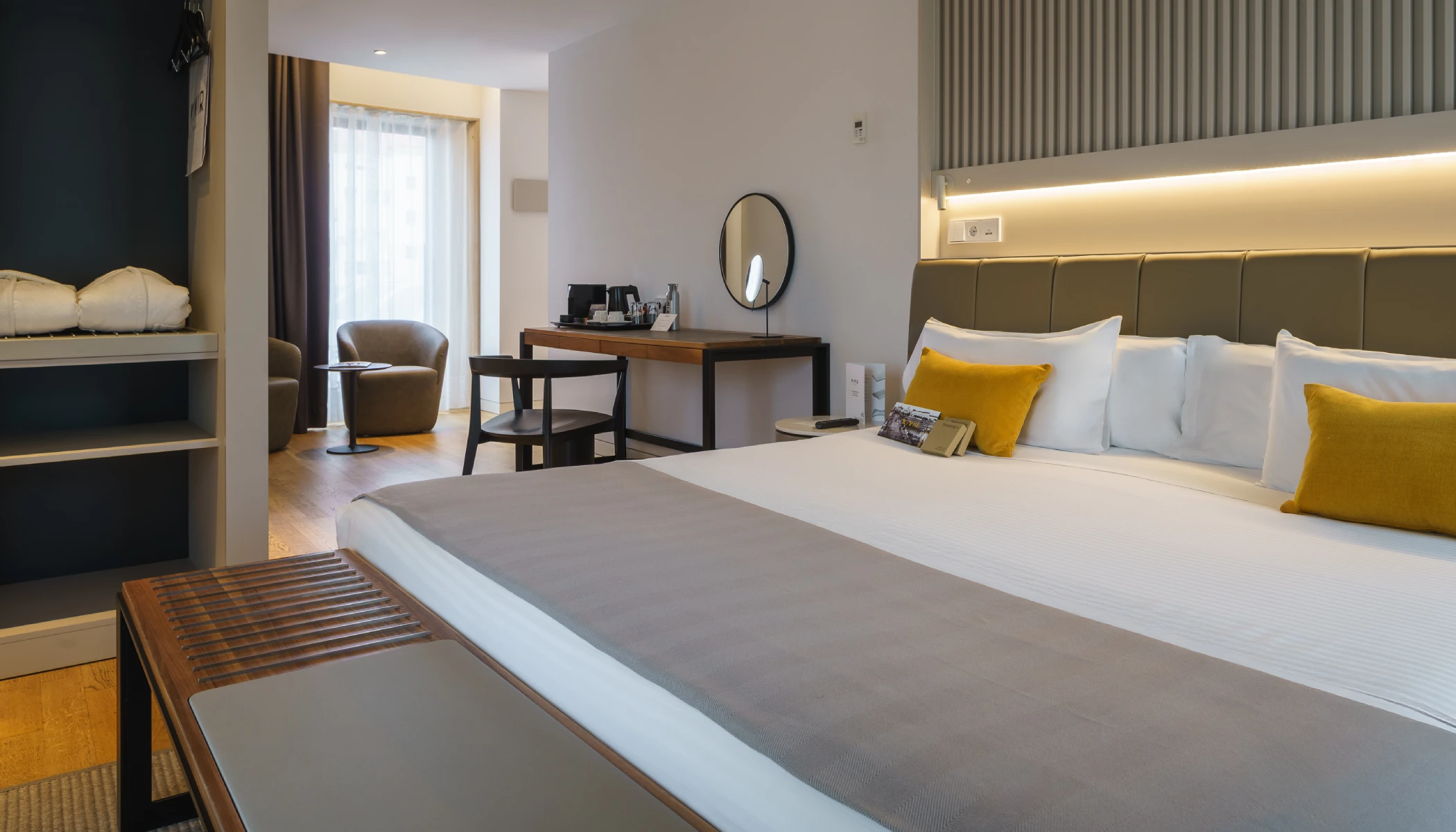 Habitaci&oacute;n de hotel moderna con cama, escritorio y sill&oacute;n cerca de la ventana.