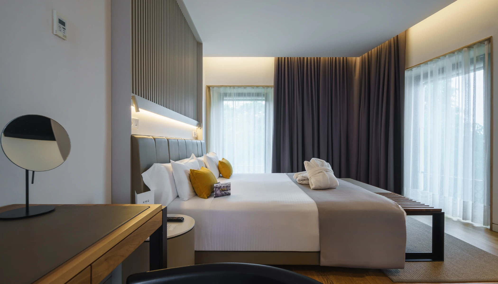 Habitaci&oacute;n moderna con cama, escritorio y cortinas oscuras.