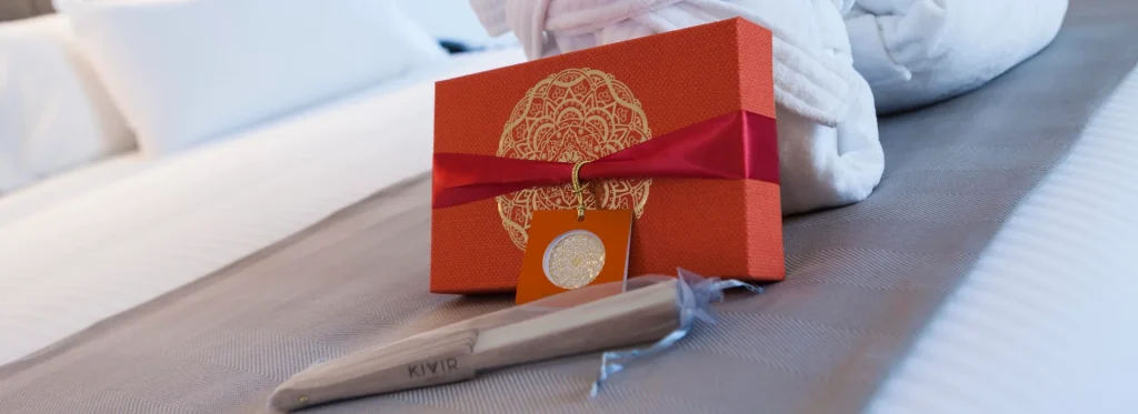 Caja de regalo naranja con cinta roja sobre una cama, junto a una navaja.