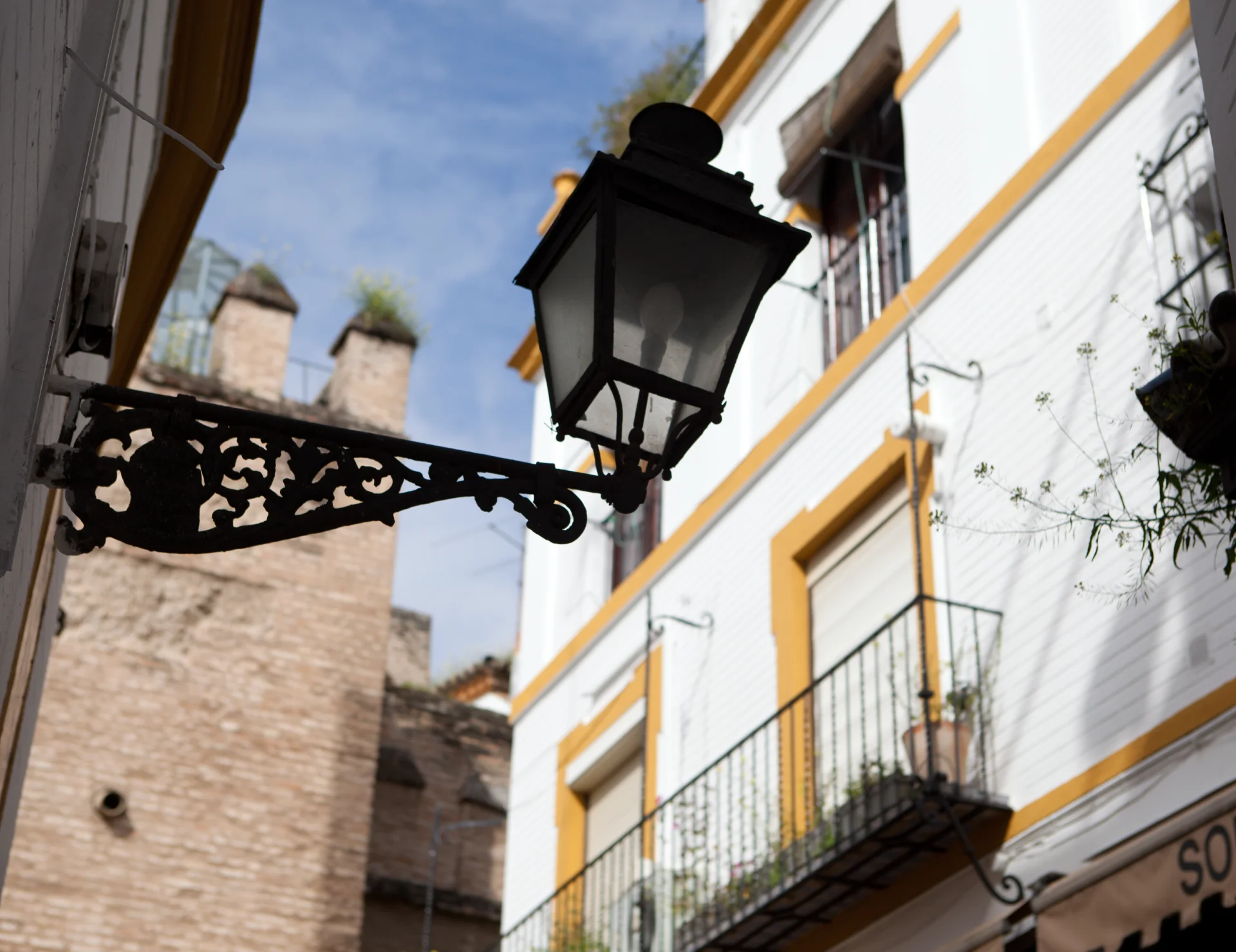 Farol colgante en una calle con edificios de balcones y cielo azul.