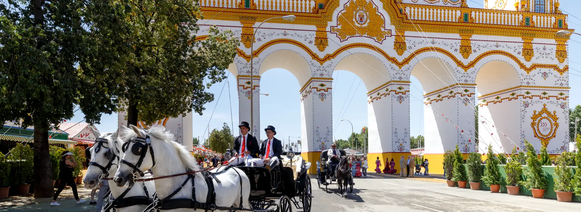 Carroza con caballos blancos pasa bajo un arco decorado en una feria.