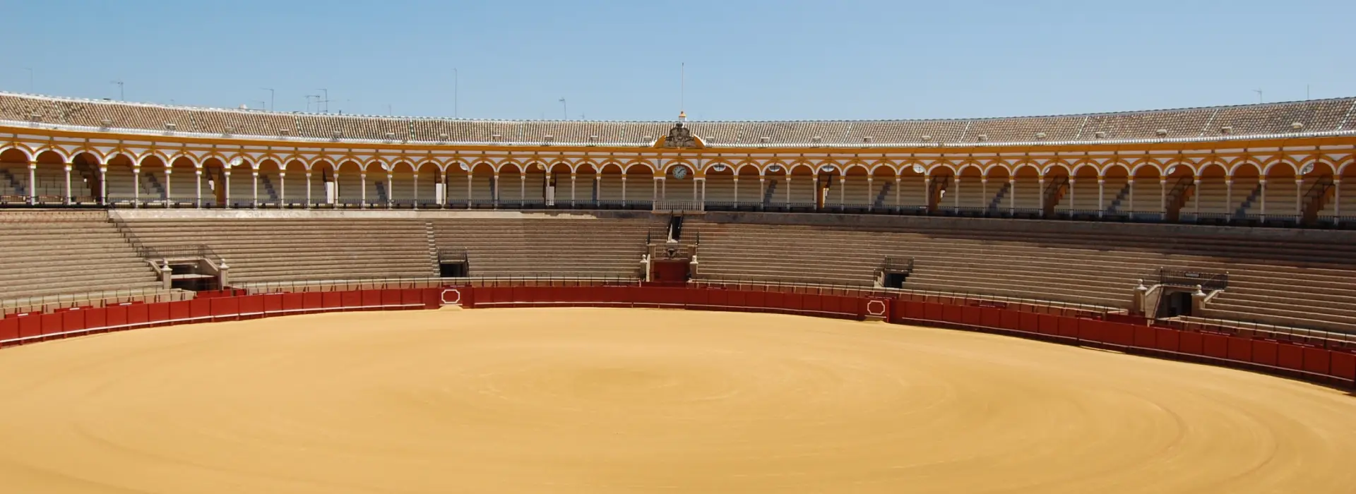 Plaza de toros vac&iacute;a con gradas circulares y cielo despejado.