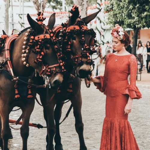 Mujer en vestido rojo junto a dos caballos adornados.