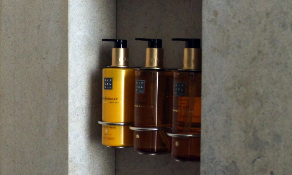Tres botellas de productos de ba&ntilde;o sobre una repisa de color claro.