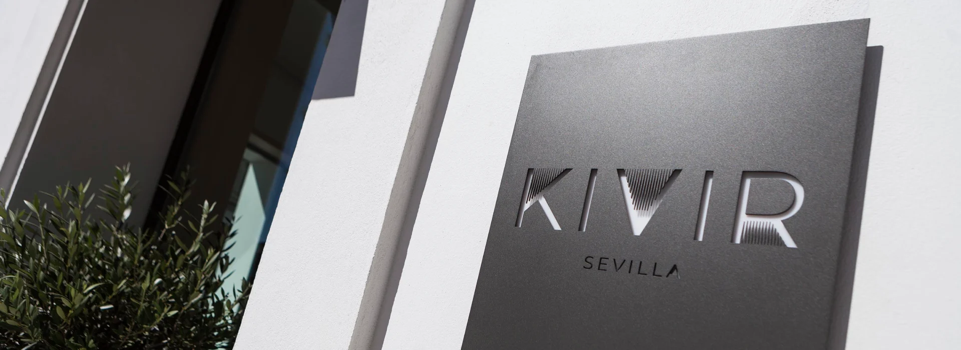 Placa negra con texto "KIVIR SEVILLA" en una pared blanca.