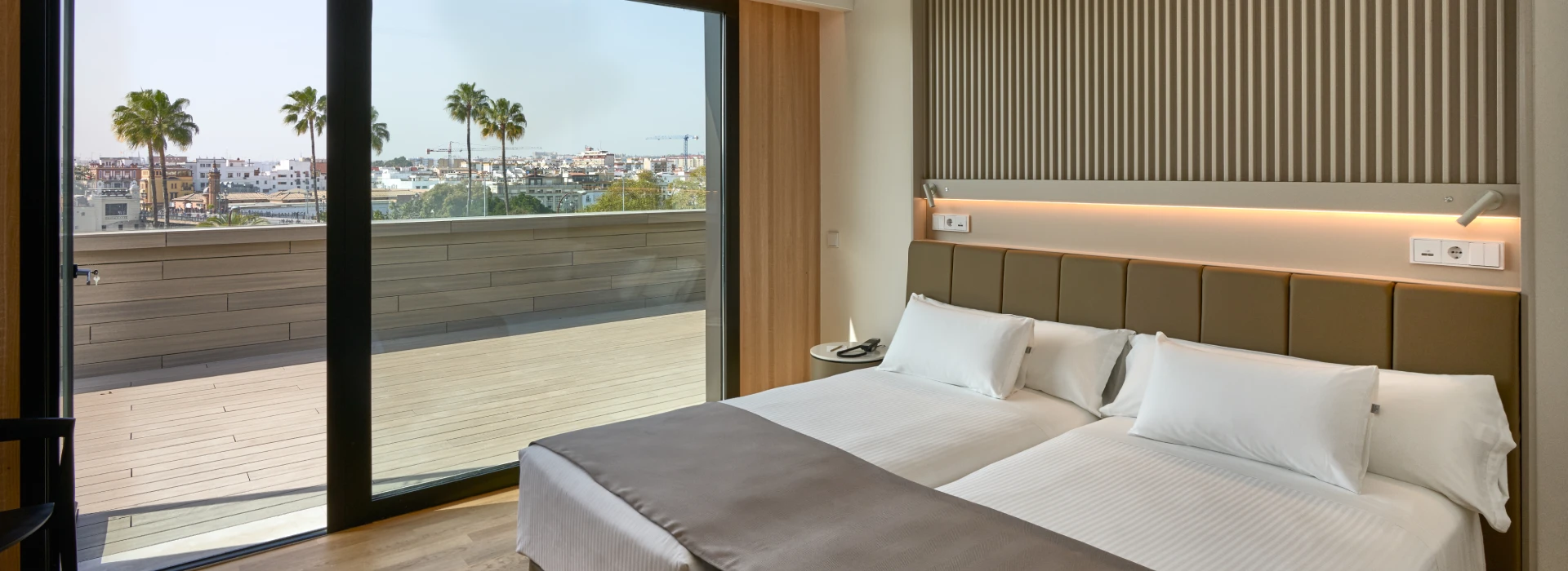 Habitaci&oacute;n moderna con terraza y vista a la ciudad y palmeras.