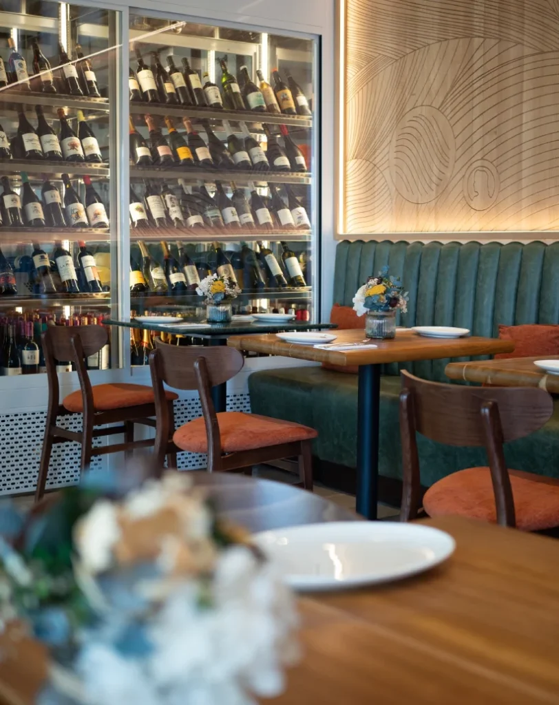 Restaurante con botellas de vino, mesas y sillas de madera.