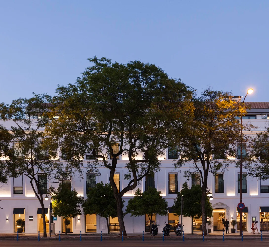 Edificio blanco iluminado con &aacute;rboles al frente al atardecer.