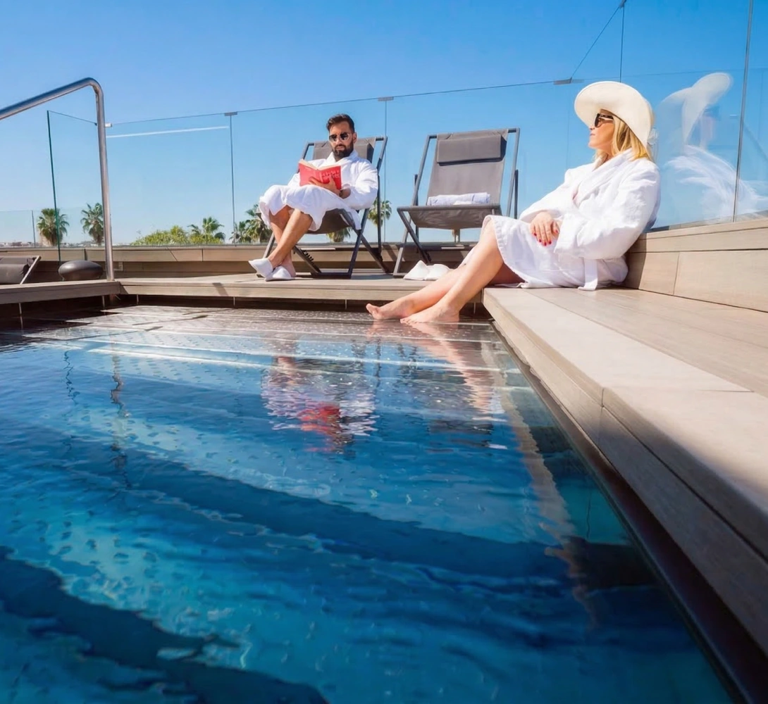 Personas relaj&aacute;ndose junto a una piscina en una terraza soleada.