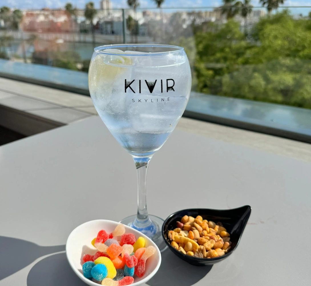 Copa de bebida con lim&oacute;n, gominolas y frutos secos en terraza con vista.